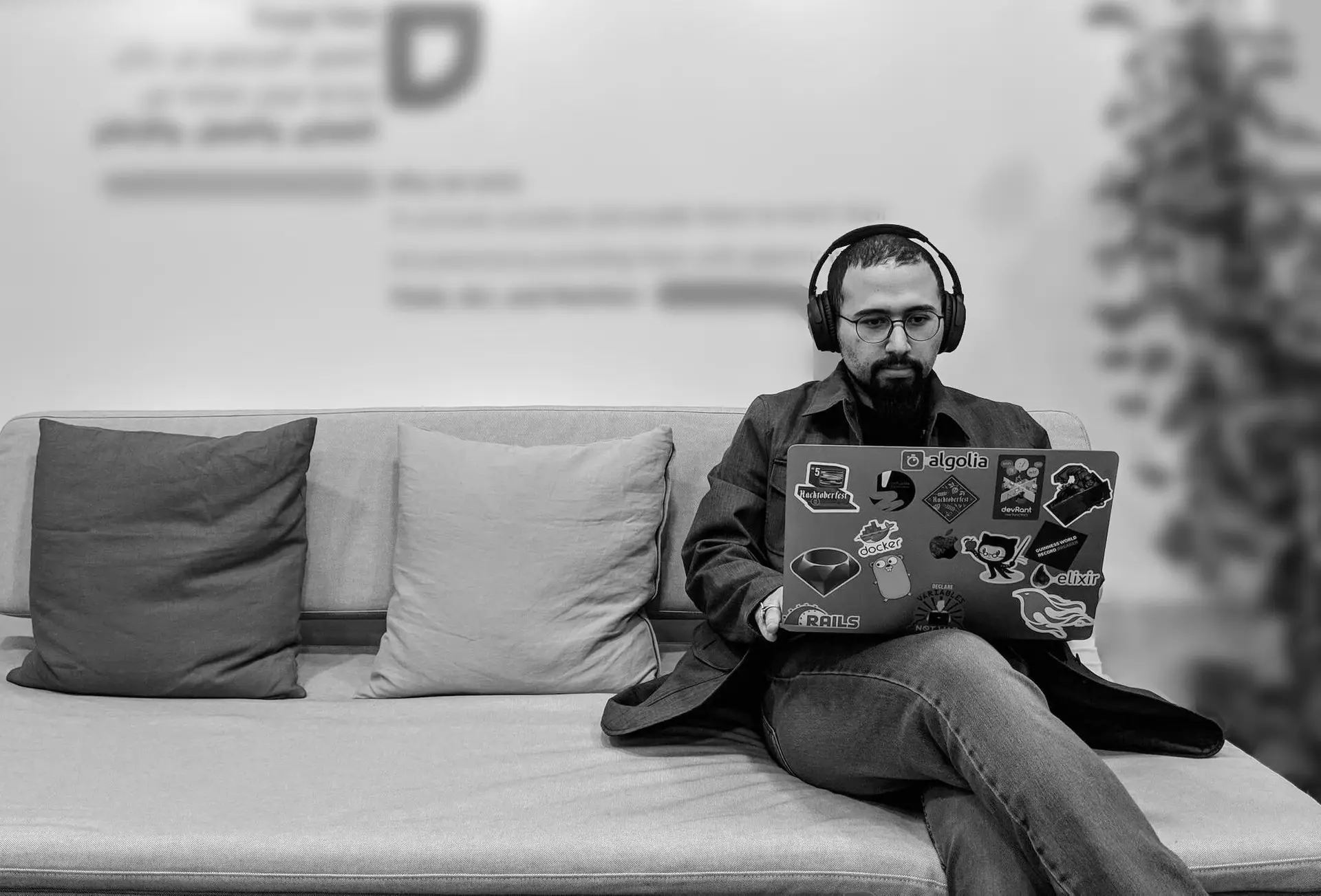 Omar working on a sticker-covered laptop, wearing headphones, seated on a couch